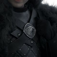 a person wearing a black coat with a silver buckle on their chest and gloves over their shoulders