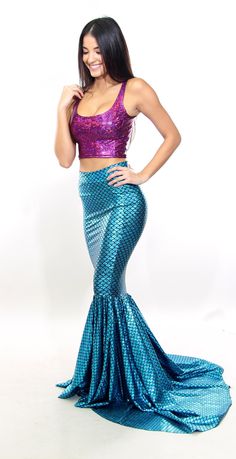 a woman in a purple top and blue mermaid skirt posing for the camera with her hands on her hips