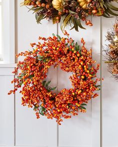 two wreaths hanging on the side of a door with orange berries and green leaves