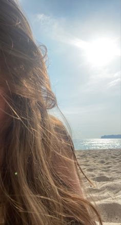 a close up of a person on a beach with the sun shining through her hair