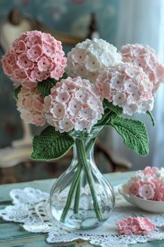 pink and white flowers in a glass vase on a table next to a lace doily