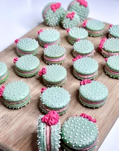 a wooden cutting board topped with cookies covered in green frosting and pink ribbon bows