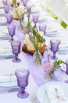 the table is set with purple glassware and flowers in vases, candles, and napkins