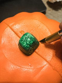 a person is carving a piece of green marble on an orange pumpkin with a knife