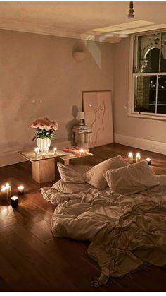 a bedroom with candles on the floor and an unmade bed in front of a window