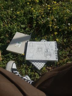 someone is sitting in the grass with their feet up next to books and notebooks