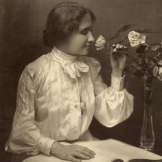 an old black and white photo of a woman sitting at a table with flowers in front of her