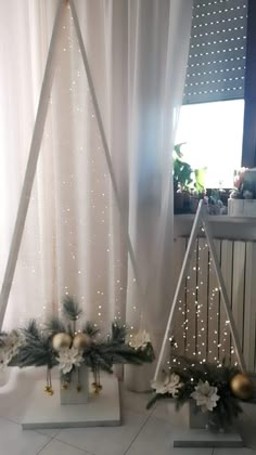 two christmas decorations are on display in front of a window with white curtains and lights