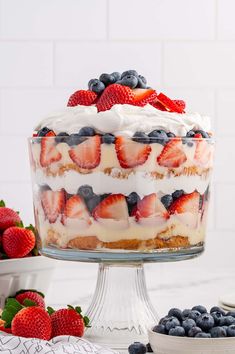 a cake with strawberries and blueberries on top is sitting on a glass stand