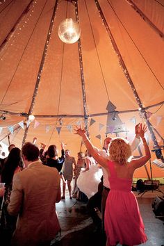 a woman in a pink dress dancing under a large tent with lights on the ceiling