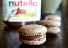 two cookies with chocolate frosting are on a table next to a jar of peanut butter