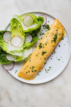 a white plate topped with lettuce and an omelet next to a salad