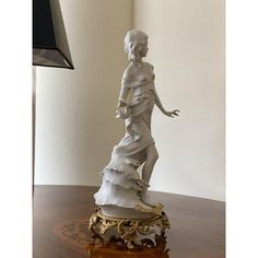 a white statue sitting on top of a wooden table next to a lamp and clock