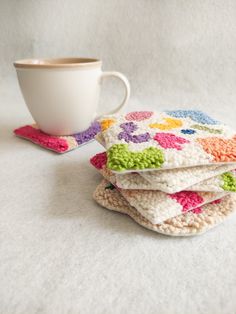 four crocheted coasters and a coffee cup on a white tablecloth with a mug in the background