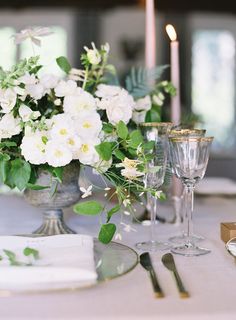 the table is set with white flowers and greenery in vases, silverware, and wine glasses