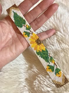 a hand is holding a beaded bracelet with yellow flowers and green leaves on it