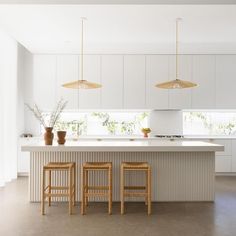 two wooden stools sit in front of an island with white cabinets and countertops