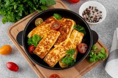 some food is in a black pan on a cutting board next to tomatoes and parsley