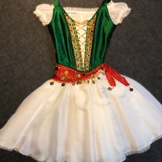 a white dress with green and red trimmings on the waist, sitting on a gray surface