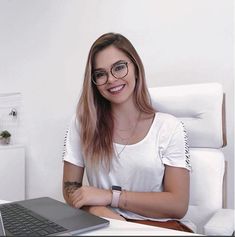 a woman sitting at a desk with a laptop computer in front of her, smiling