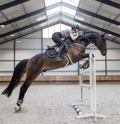 a woman riding on the back of a brown horse over an obstacle in a building