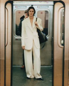 a woman in white suit standing at the door of a subway train with her hand on her hip