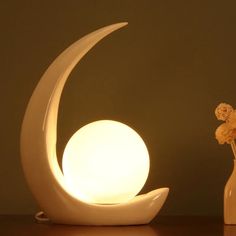 a vase with flowers in it next to a lamp on a table that looks like the moon