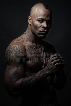 a shirtless man with tattoos on his chest and hands clasped in front of him