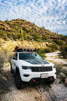 a white jeep is parked on the side of a dirt road with cactus in the background