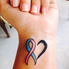 a woman's wrist tattoo with a pink and blue ribbon on the left hand