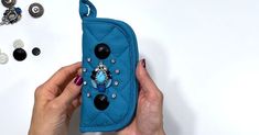 a hand holding a blue case with buttons on it and some other accessories around it