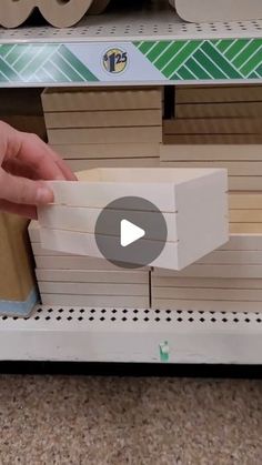 a person is holding a piece of wood in front of a shelf with other items