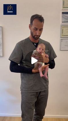 a man holding a baby in his arms while standing next to a wall with pictures on it