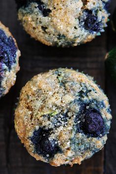 two blueberry muffins sitting next to each other on a wooden surface with an avocado in the background