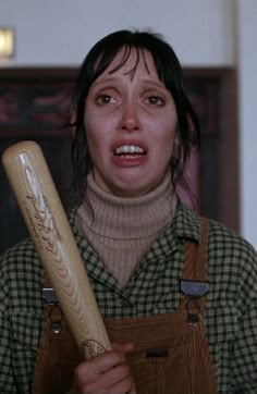 a woman holding a wooden baseball bat in her right hand and looking at the camera