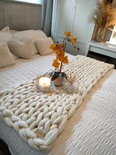 a bed with a white blanket on top of it and some flowers in the middle