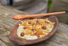 a small pizza with toppings is on a wooden plate next to an orange spoon