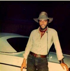 a man wearing a hat standing next to a white car