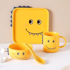 a yellow plate with two mugs and spoon next to it on a white table