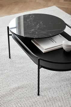 a black table with a book on it and a white bowl next to it in front of a rug