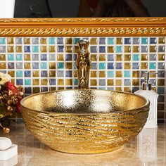 a gold bowl sink sitting on top of a counter next to a vase with flowers