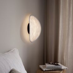 a bedroom with a white bed and a round light fixture on the wall above it