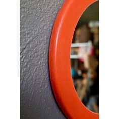 an orange circle hanging on the side of a gray wall with people in the background