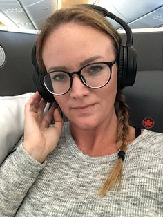 a woman wearing headphones while sitting in an airplane with her hand on her ear