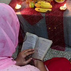 a woman sitting down reading a book in front of some bananas and other fruit on the table