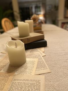 two candles sitting on top of an open book next to some folded up papers and books