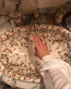 a woman is washing her hands in the bathroom sink with floral designs and gold faucets