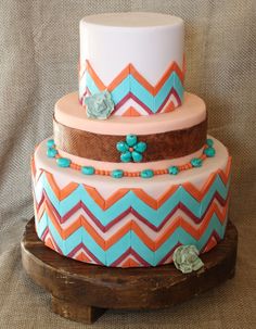 a three tiered cake decorated with blue, orange and pink chevrons on a wooden stand