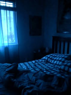 a bed in a dark room with blue light coming through the window