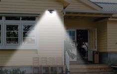 a light shines on the side of a house in front of a porch with chairs